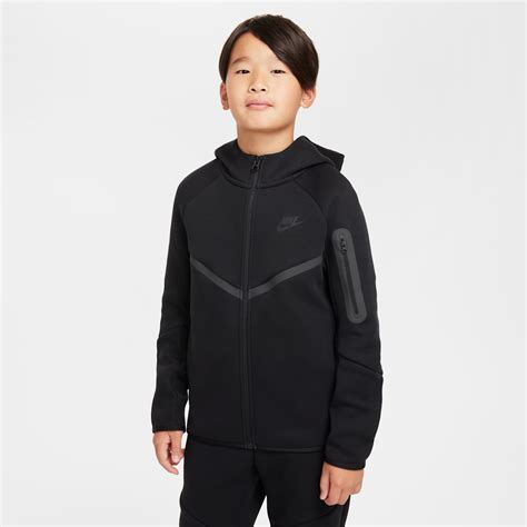 Niño sonriendo mientras lleva una sudadera con capucha Nike Tech Fleece, destacando el diseño y la comodidad.