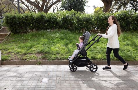 Fotografía de una madre caminando con su bebé en el cochecito en un parque, sonriendo.