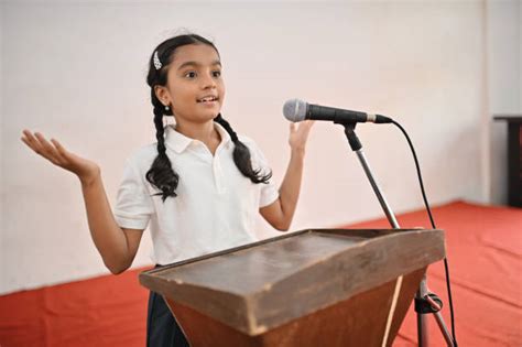 Niña dando un discurso en un podio con micrófono, mostrando confianza y seriedad.