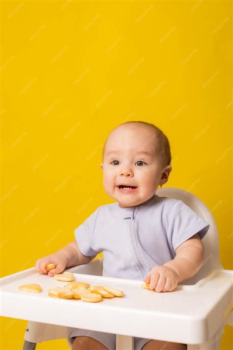 Bebé comiendo una galleta casera en una trona, con ingredientes frescos en el fondo