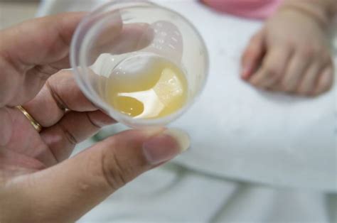 Fotografía de una madre extrayendo calostro con una jeringa en un entorno hospitalario.