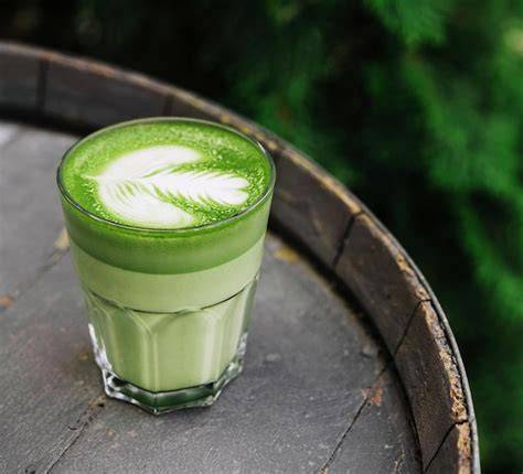Taza de matcha latte humeante con espuma y polvo de matcha espolvoreado