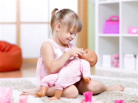 Foto de una niña jugando con una muñeca bebé y un biberón de juguete