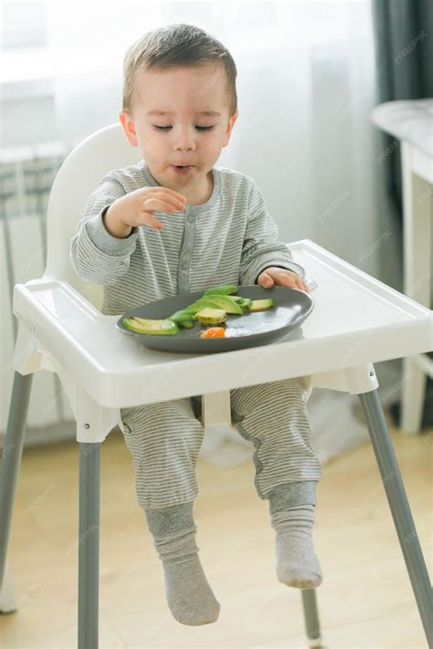 Bebé sentado en silla alta comiendo trozos de fruta con las manos, enfoque BLW