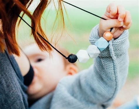 Bebé interactuando con un collar de lactancia mientras la madre lo sostiene