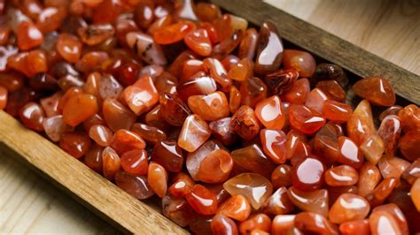 Composición artística que muestra diferentes piedras naturales (Piedra Luna, Cuarzo Rosa, Cornalina, Jaspe Rojo, Rodocrosita) dispuestas alrededor de un símbolo de fertilidad femenina, con un fondo suave y natural.