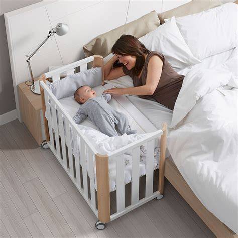 Foto de bebé durmiendo plácidamente en una minicuna de colecho junto a la cama de los padres
