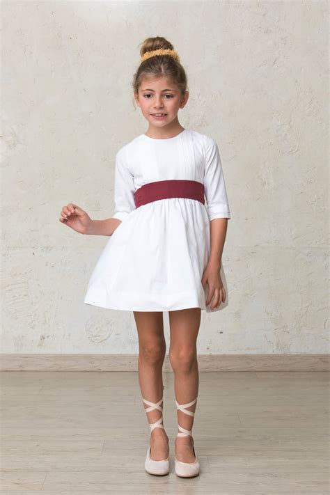 Niña con vestido blanco y cubrepañal a juego en un evento formal.