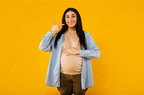 Mujer embarazada sonriendo y tocando su vientre en un campo soleado, representando felicidad y serenidad