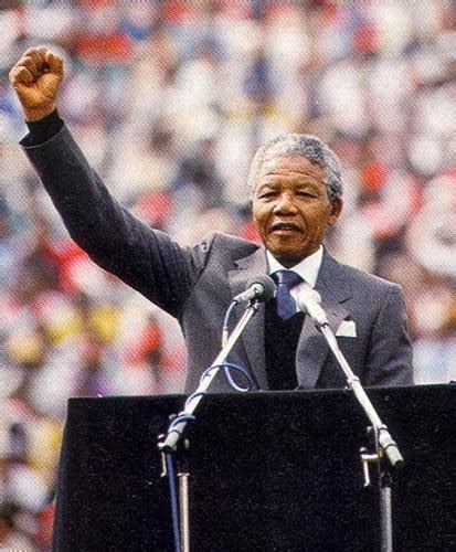 Imagen de Nelson Mandela dando un discurso durante su presidencia, rodeado de miembros de su gabinete.