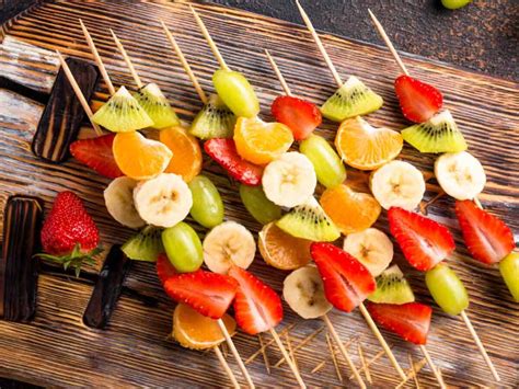 Brochetas de fruta coloridas y vasos reutilizables en una mesa de fiesta.