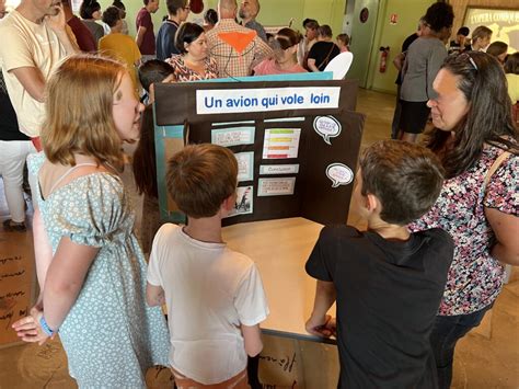 Fotografía del Village des Sciences en la sala Osco Manosco con stands interactivos y estudiantes participando en experimentos científicos.