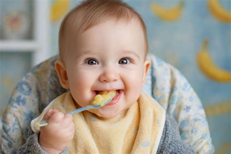 Bebé sonriente disfrutando de su primera papilla de frutas, un momento clave en la transición a sólidos.