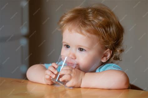 Bebé bebiendo agua de un vaso pequeño abierto con la ayuda de un adulto
