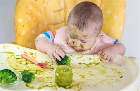 Imagen de un bebé jugando con su comida en la trona, mostrando el aspecto de la exploración táctil.