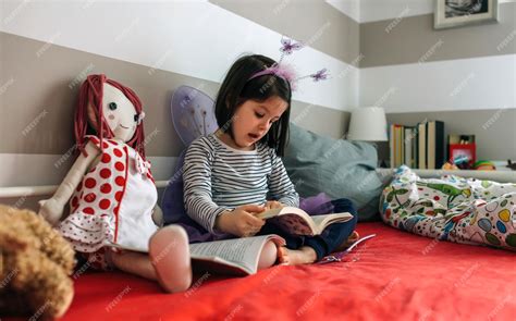 Niña pequeña disfrazada de mariposa leyendo un libro a su muñeca de trapo