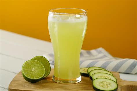 vaso de agua con rodajas de limón y pepino, junto a un plato de frutas frescas