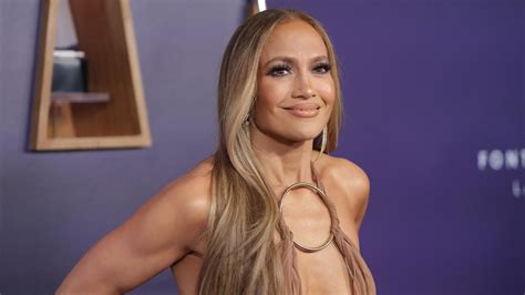 Joven Jennifer Lopez sonriendo, con un micrófono en la mano, vestida de forma casual