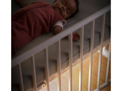 Foto de la luz de cuna Glow de Maxi-Cosi instalada debajo de una cuna, emitiendo una luz suave