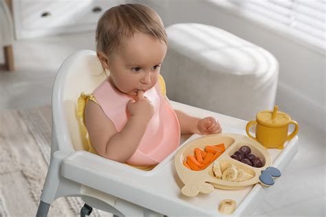 Bebé con babero disfrutando de trozos de fruta y verdura, destacando la importancia de la autonomía en la mesa.