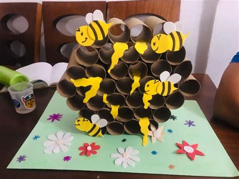 Infografía detallada con los pasos para crear una abeja con rollos de papel higiénico, mostrando los materiales y el resultado final.