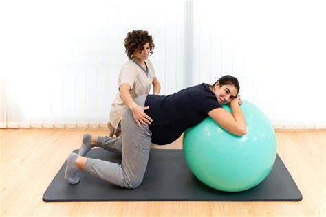 Mujer embarazada de rodillas con las manos sobre la pelota de pilates y una pierna adelantada, movilizando la pelvis.