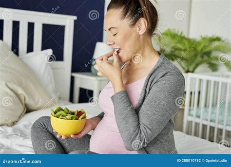 Foto temática de una mujer embarazada comiendo un bol de frutas y yogur.