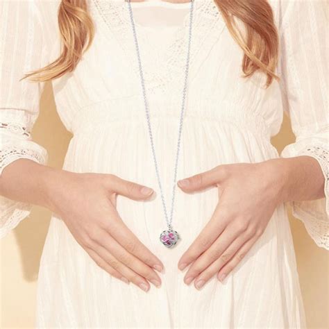 Fotografía artística de una mujer embarazada luciendo un collar largo con un llamador de ángeles de plata sobre su vientre.