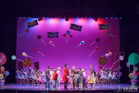 Fotografía de un escenario de teatro infantil con una escenografía colorida y niños en el público atentos al espectáculo.