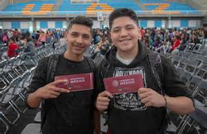 Estudiante joven celebrando una beca de estudios superiores, con su madre de fondo en un puesto de arepas.
