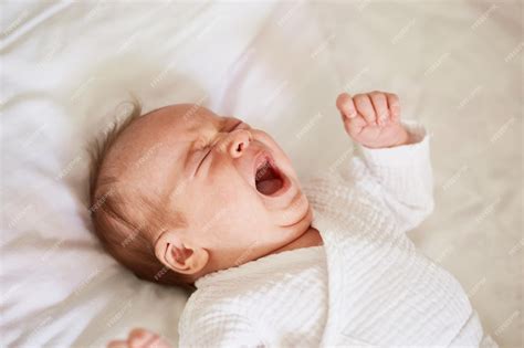 Bebé recién nacido llorando en la cuna mientras un padre lo mira con preocupación
