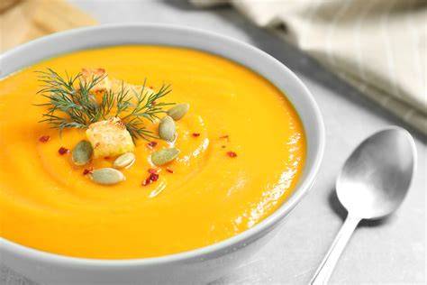 Fotografía cenital de una crema de calabaza servida en un bol con un toque de semillas y aceite de oliva