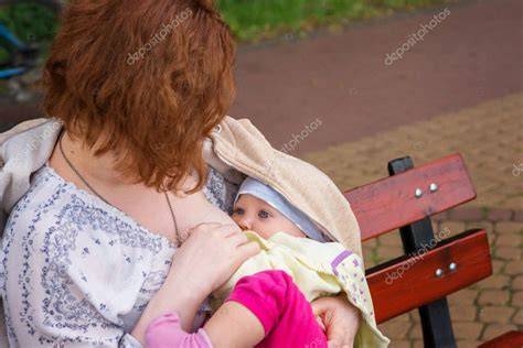 Madre amamantando a su bebé en un parque, con otras personas alrededor