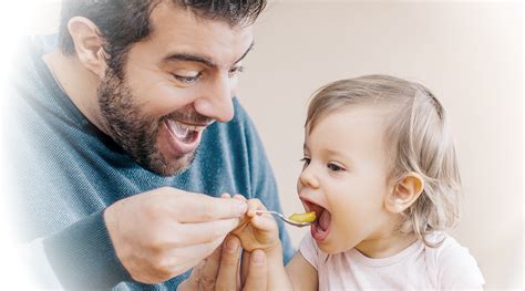 Padre amoroso limpiando la cara de su bebé mientras come papilla, con una atmósfera relajada y sonriente.