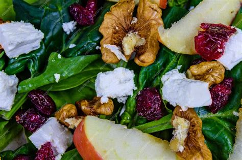 Primer plano de una ensalada colorida con queso feta desmenuzado, pasas, nueces y hojas verdes frescas.