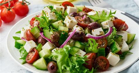 Ingredientes frescos para una ensalada mediterránea: pepino, pimiento verde, limones, maíz, pasas, queso feta y perejil.