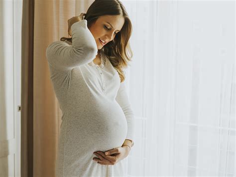 Fotografía de una mujer embarazada sonriendo, vestida con un elegante traje de invitada.