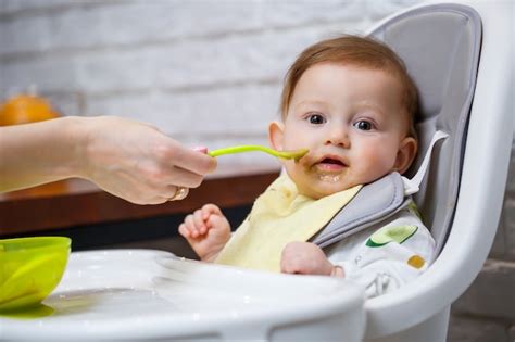 Bebé sentado en una trona, explorando alimentos sólidos con sus manos.