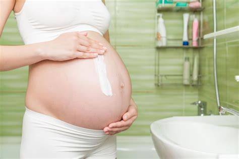 Mujer embarazada aplicando crema en el abdomen