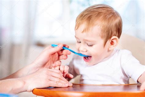 bebé sonriendo mientras come papilla de cereales de una cuchara, con su padre ayudando