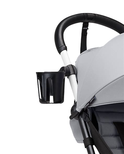 Imagen de un portavasos acoplado al manillar de un cochecito de paseo, mostrando un biberón o taza en su interior.