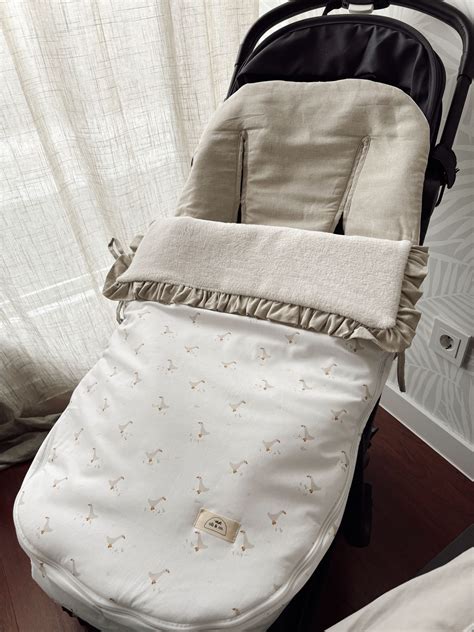 Fotografía de alta calidad de un saco de silla de paseo confeccionado en piqué con detalles de lazos y acabados textiles.