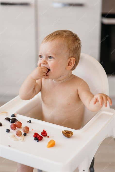 Bebé sentado en una trona comiendo trozos de fruta con las manos