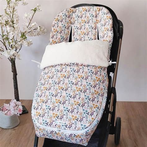Fotografía de un bebé en un saco de silla de paseo de color rojo, con detalles de cintas beige
