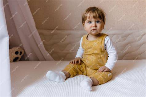 Niño pequeño sentado en el borde de una cama baja, sonriendo