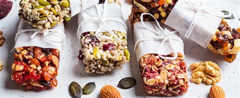 Variedad de snacks saludables en cuencos pequeños: frutos secos, fruta fresca cortada, hummus con palitos de zanahoria, barras de cereales.