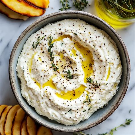 Cuenco con dip cremoso de queso feta decorado con hierbas y limón