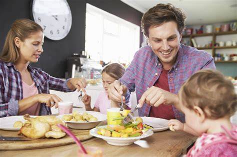 Familia comiendo junta, con el bebé sentado en la trona explorando sus alimentos