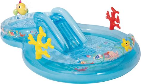 Bebé jugando en una pequeña piscina inflable bajo una sombrilla en la playa
