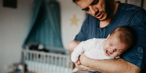 Bebé con expresión de malestar por cólicos, siendo sostenido por un padre